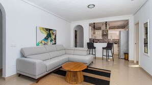 Una sala de estar moderna con un sofá seccional gris, una mesa de centro de madera y un cuadro abstracto de colores en la pared.