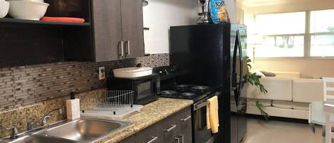 A modern kitchen with dark cabinetry, a granite countertop, stainless steel sink, and a black stove.