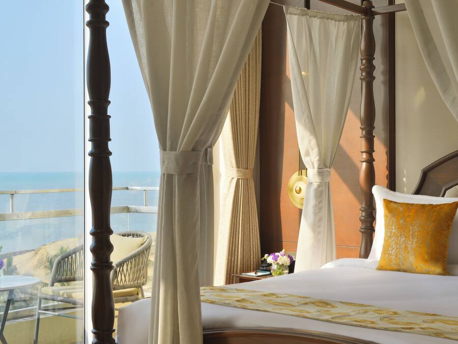 A bedroom with a bed, curtains, a nightstand, and a view of the ocean.
