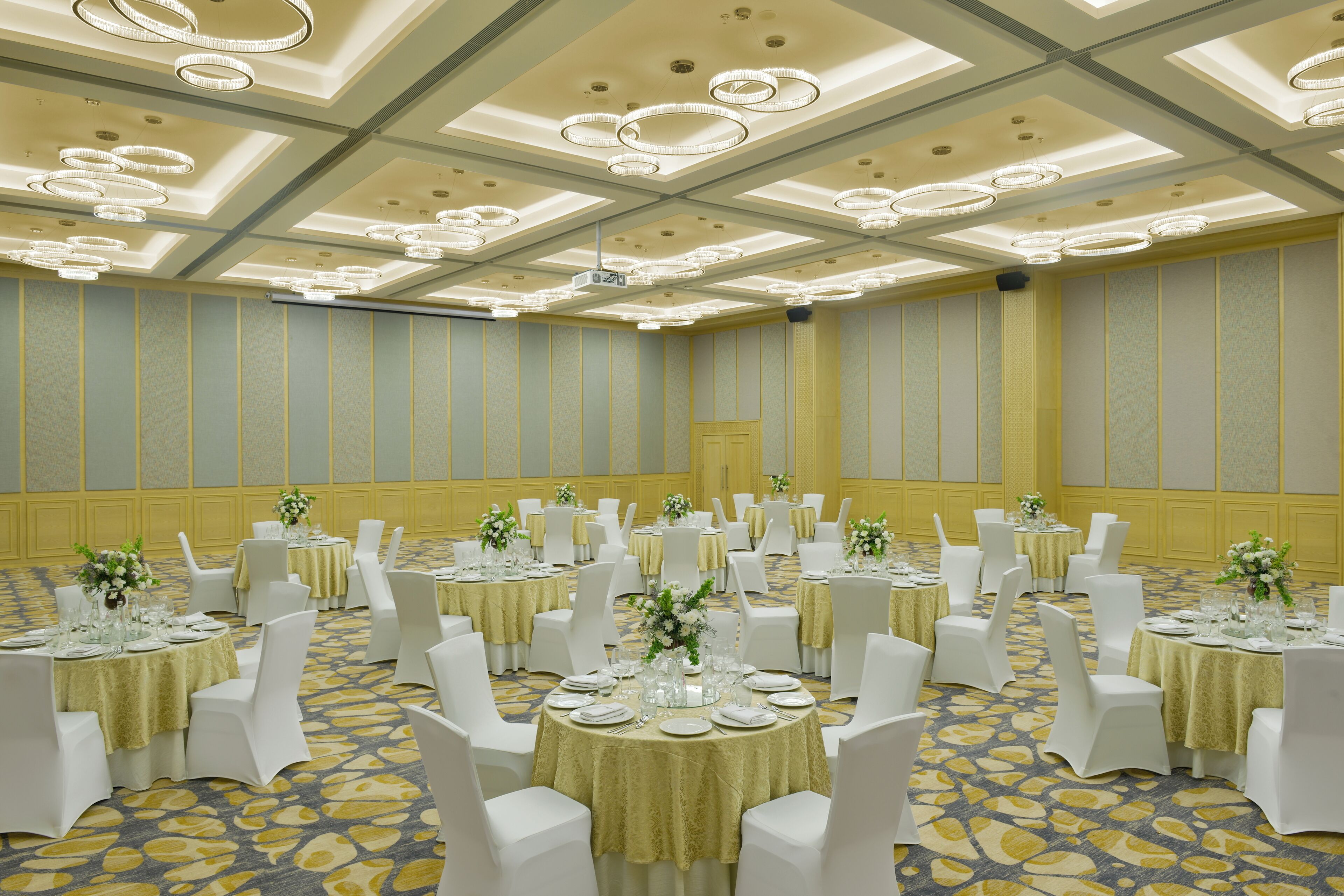A banquet hall with round tables, white chairs, and floral centerpieces.