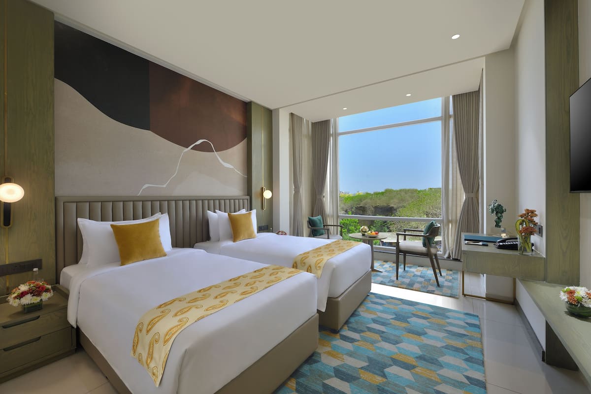 A hotel room with two beds, a desk, a TV, and a balcony with a view.