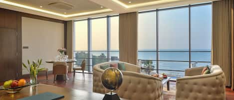 Un hotel moderno con una habitación amplia y ventana grande con vistas al mar, un sofá cómodo, un escritorio con un globo terráqueo y un comedor con vistas.