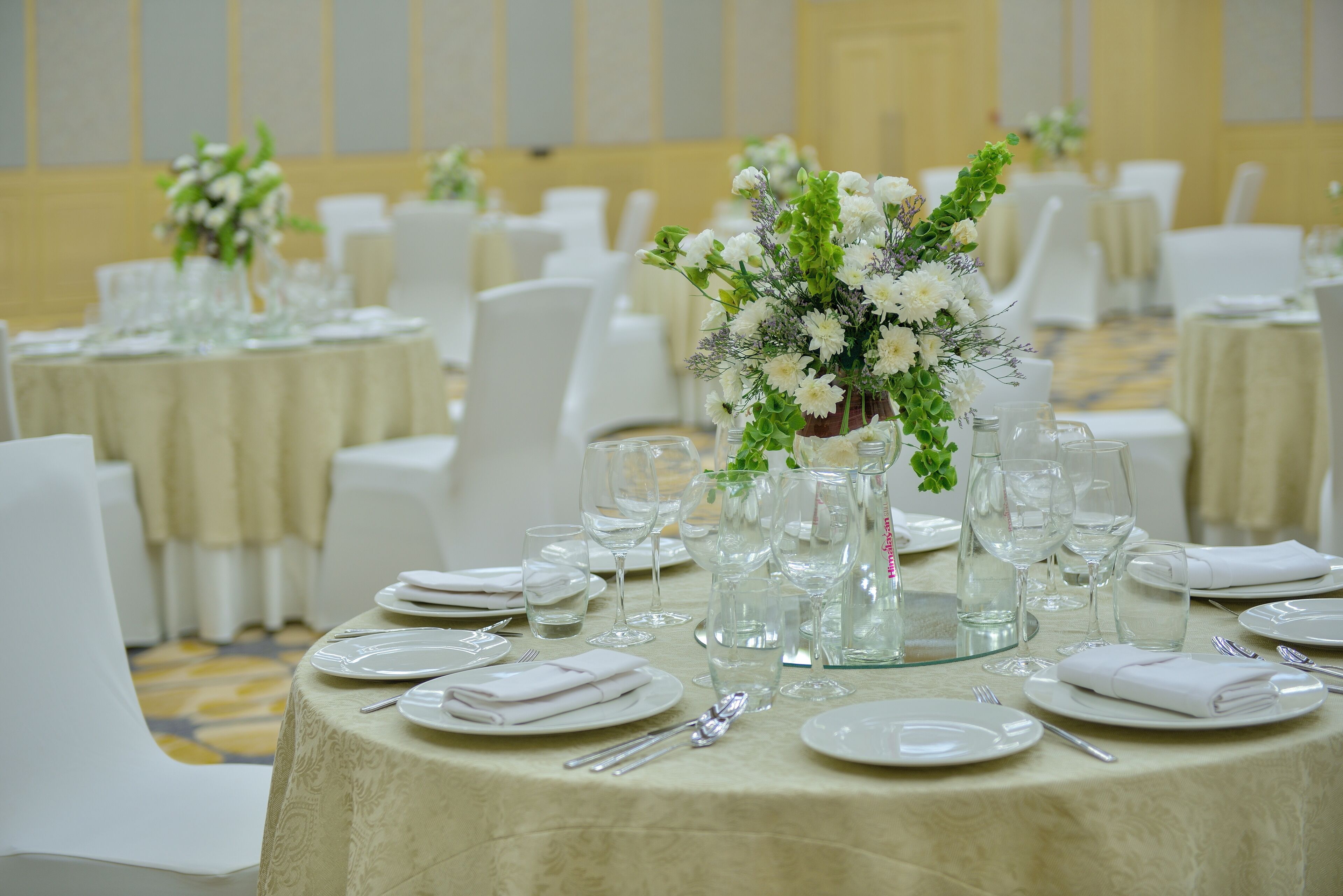 A banquet hall with round tables set for a formal event, featuring white tablecloths, glassware, and floral centerpieces.