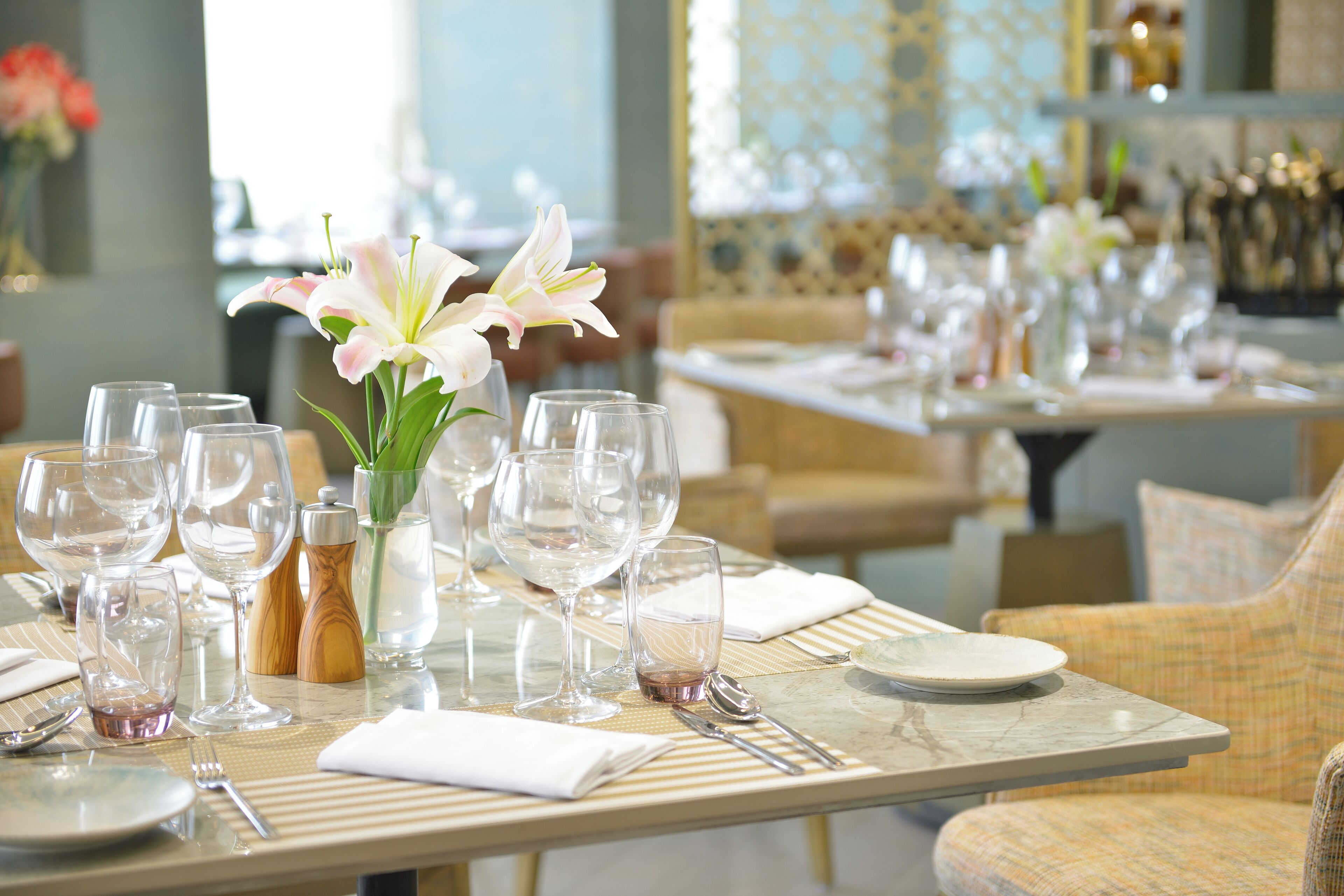 Mesa de comedor dispuesta con varias copas de vino, un jarrón con flores y cubiertos ordenados.