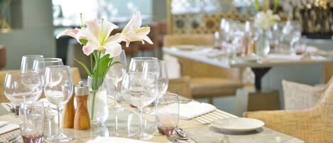 Mesa de comedor dispuesta con varias copas de vino, un jarrón con flores y cubiertos ordenados.