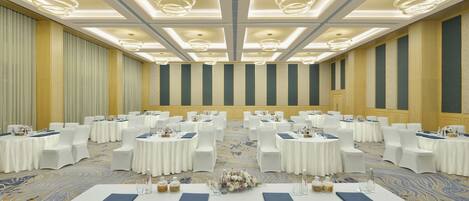 Un amplio salón de conferencias bien iluminado con mesas redondas y sillas blancas, con alfombra estampada y un techo decorativo.