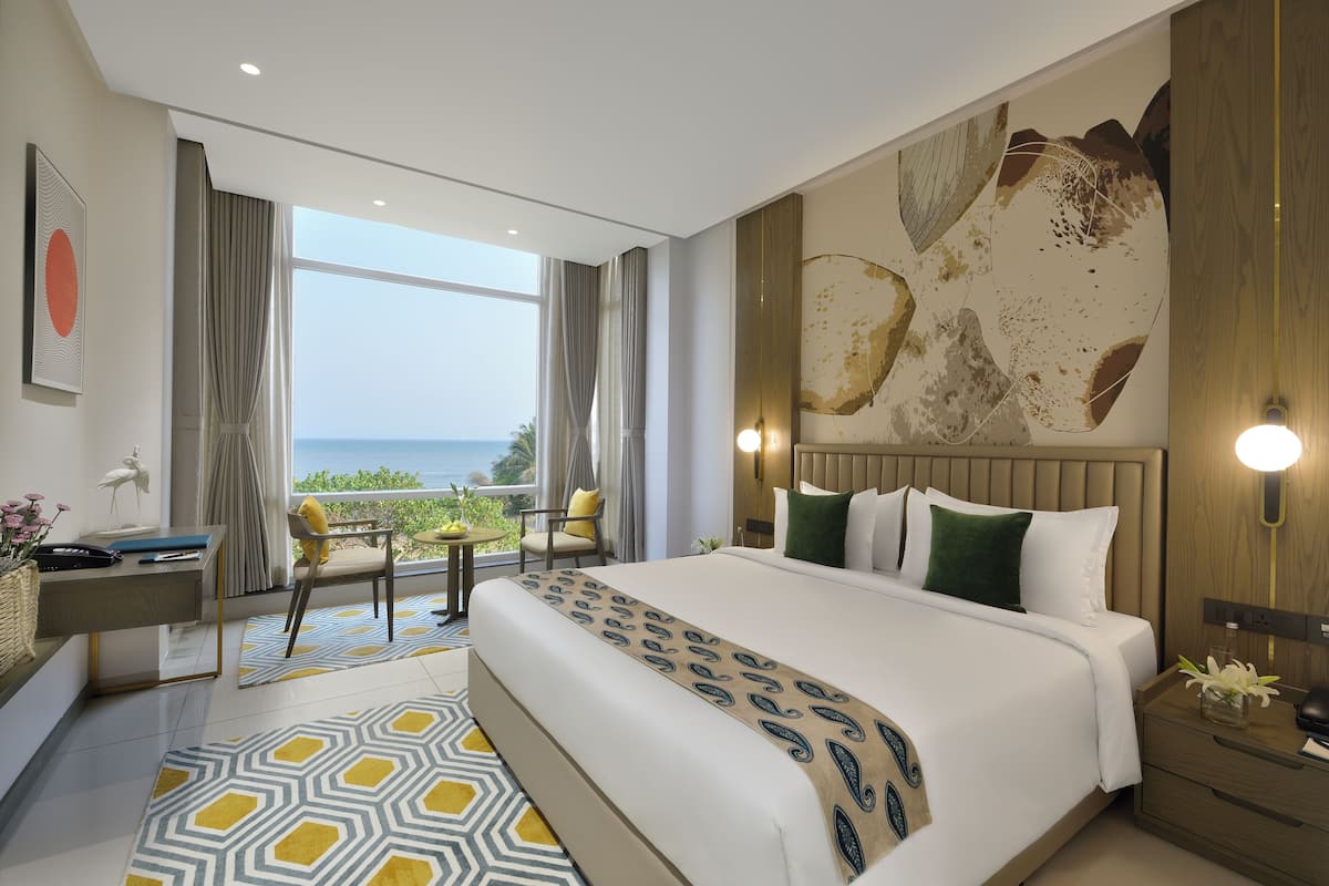 A modern hotel room with a large bed, a desk, and a view of the sea.