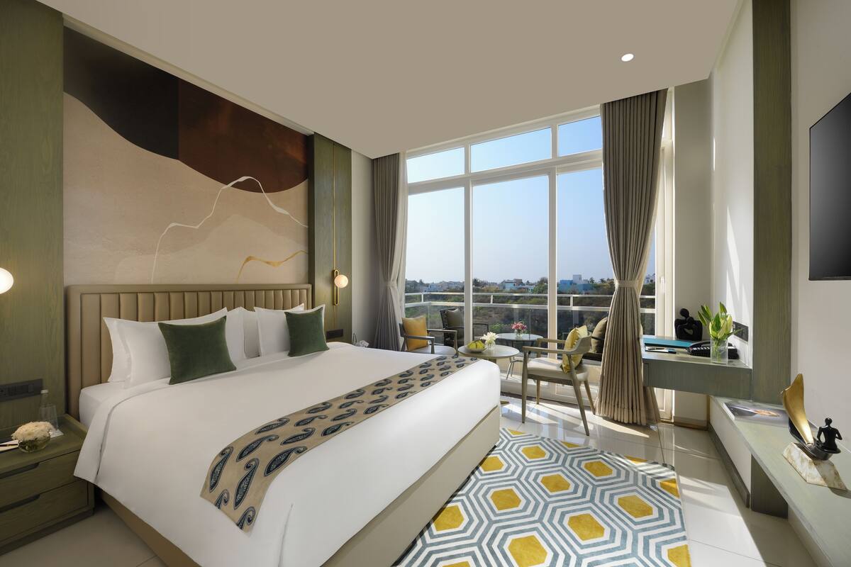 A modern hotel room with a large bed, a desk, a chair, and a view of the city.