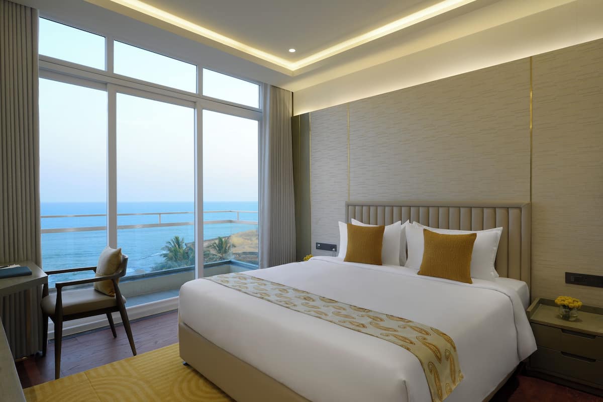 A hotel room with a large bed, a desk, and a chair. The room has a view of the ocean.