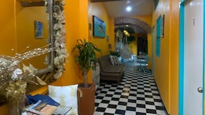 Un pasillo con piso de cuadros, paredes amarillas y un espejo con detalles decorativos.