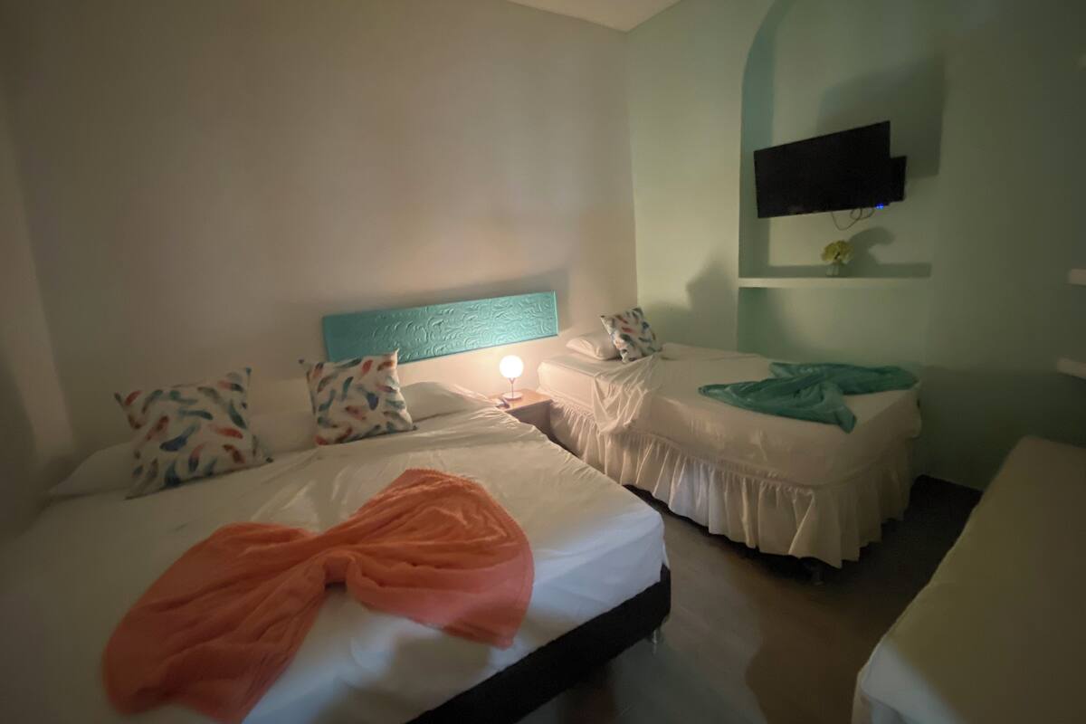Ein Hotelzimmer mit zwei Betten, einem an der Wand montierten Fernseher und einem Nachttisch mit Lampe.