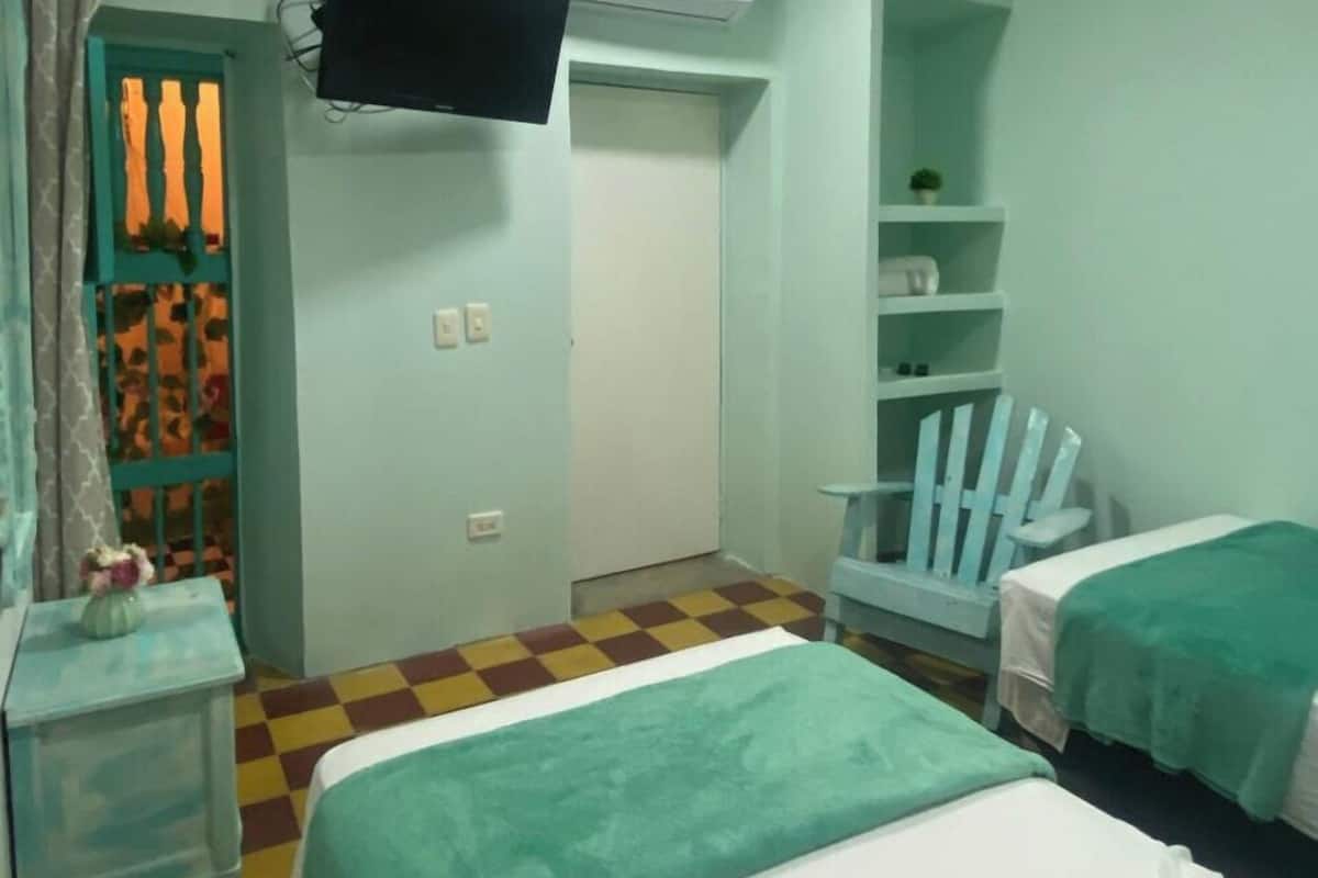 Ein Zimmer mit zwei Betten, einem an der Wand befestigten Fernseher, einem Kleiderschrank und einer kleinen Regaleinrichtung.