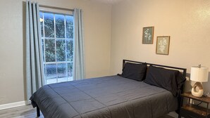 A bedroom with a large bed, a bedside table with a lamp, and two framed pictures on the wall. - Stay Longer for Less – Affordable Extended Stay (Garland)