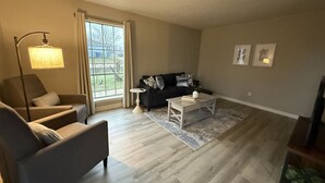 A modern living room with a sofa, armchairs, a coffee table, and a floor lamp. - Stay Longer for Less – Affordable Extended Stay (Garland)