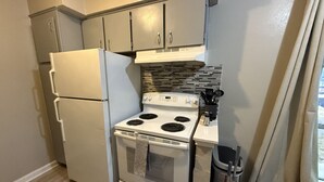A compact kitchen with a refrigerator, stove, and cabinets. - Stay Longer for Less – Affordable Extended Stay (Garland)