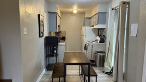 A narrow hallway with a wooden table and benches, leading to a kitchen area with a refrigerator and stove. - Stay Longer for Less – Affordable Extended Stay (Garland)