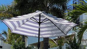 A patio area with a striped umbrella, a table, chairs, and potted plants.