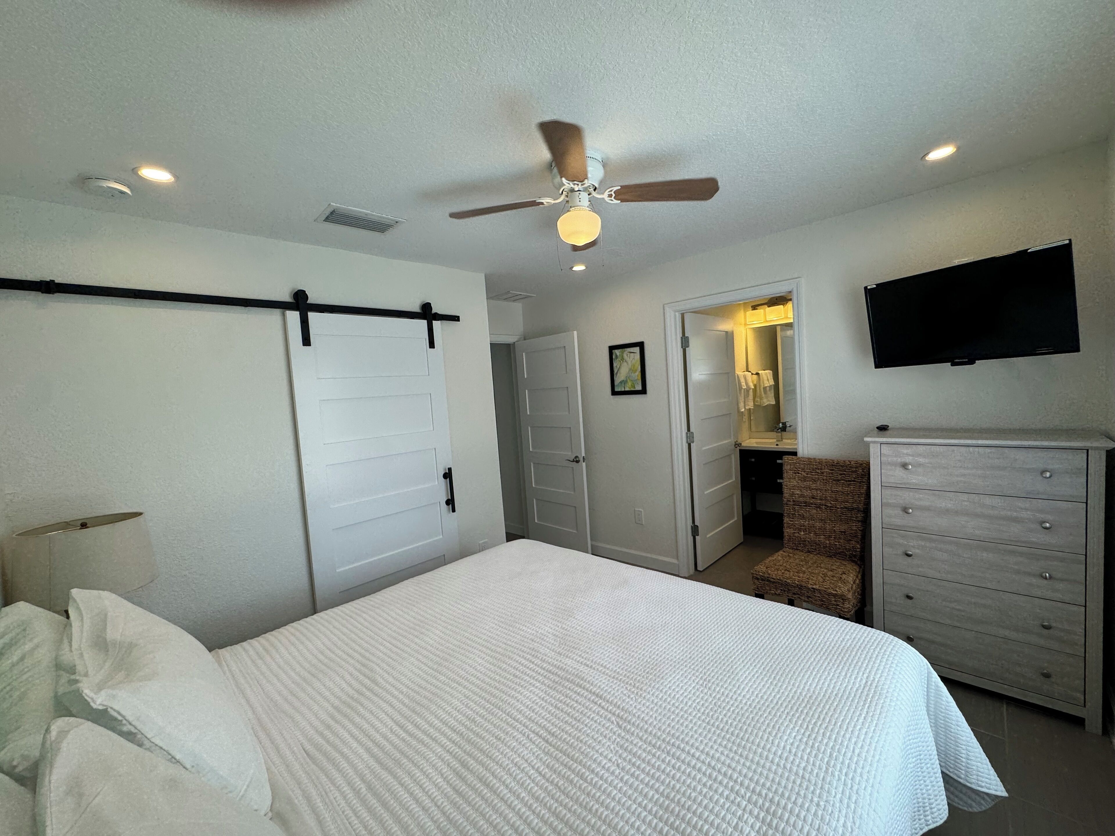 A bedroom with a bed, a dresser, a ceiling fan, and a TV.