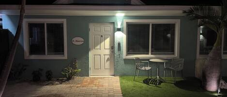 A house with a door labeled "St. Maarten," a small patio with a table and chairs, and a well-lit entrance.