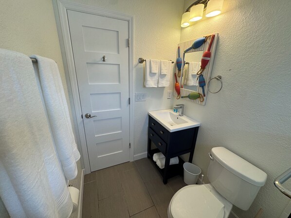 Un baño con puerta blanca, un lavabo, un inodoro y un espejo con toallero.