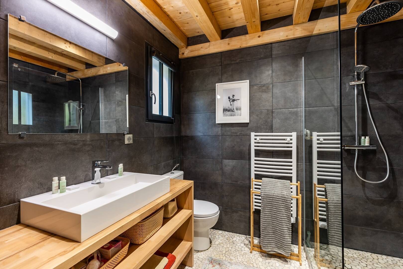A modern bathroom with a large mirror, a wooden vanity, a shower, and a toilet.