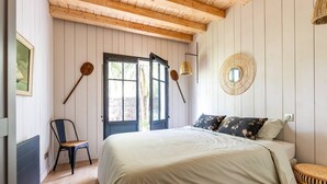 Un dormitorio con una cama grande, una silla, una mesa redonda tejida y una puerta con vista al exterior.