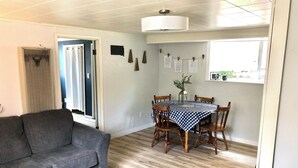 Tunnelmallinen olohuone, jossa on harmaa sohva, ruokapöytä ruutukuvioisella pöytäliinalla, puiset tuolit ja pieni ruukkukasvi.
