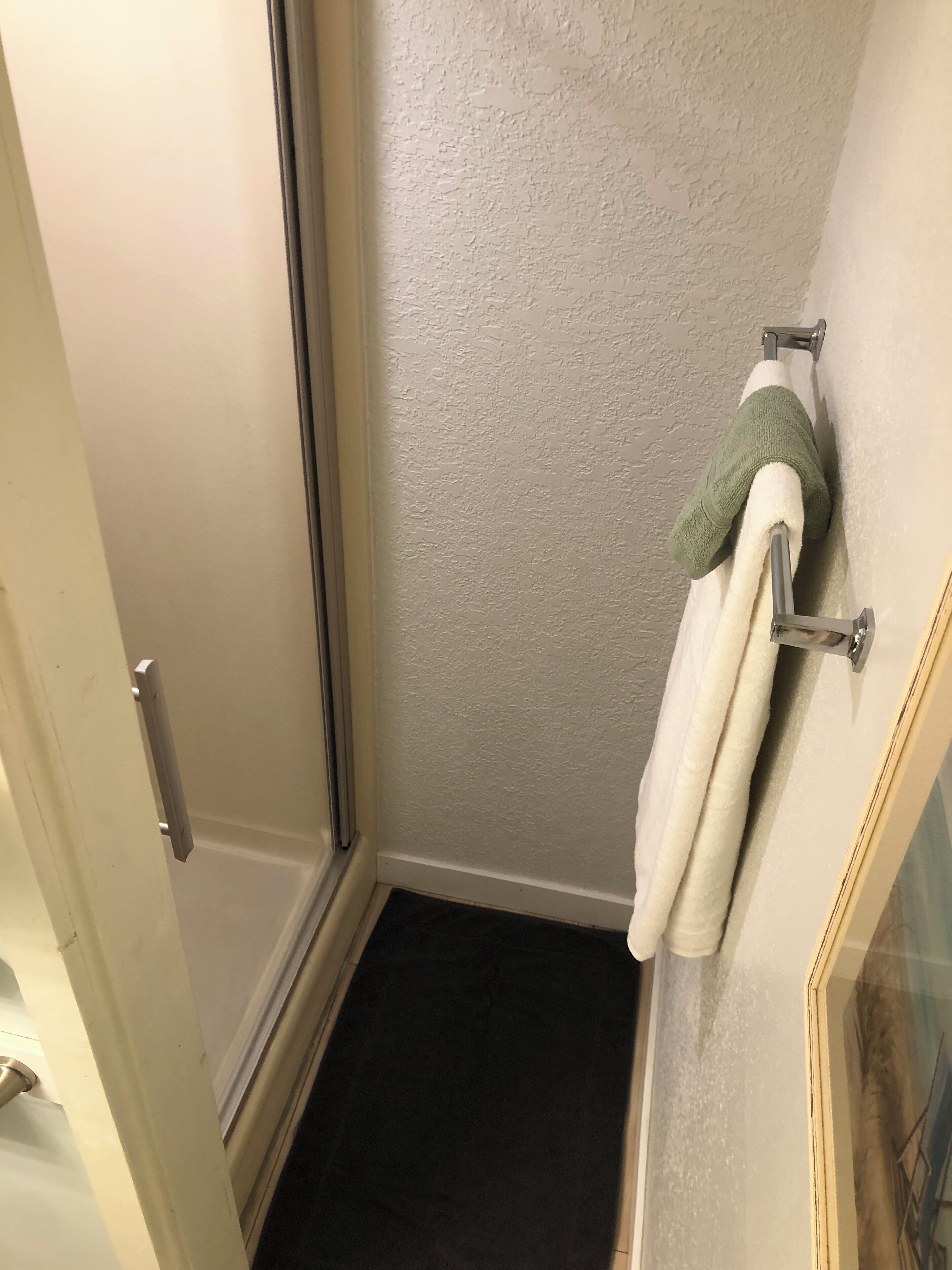 A bathroom with a white door, a towel rack with a white towel and a green towel, and a dark floor.