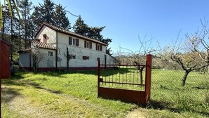 Una casa de dos pisos con techo de tejas rojas, patio cercado y cielo despejado.