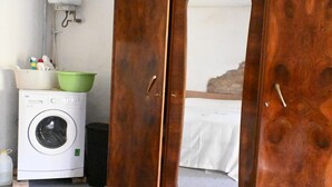 Una habitación con lavadora, espejo y cama con sábana blanca.