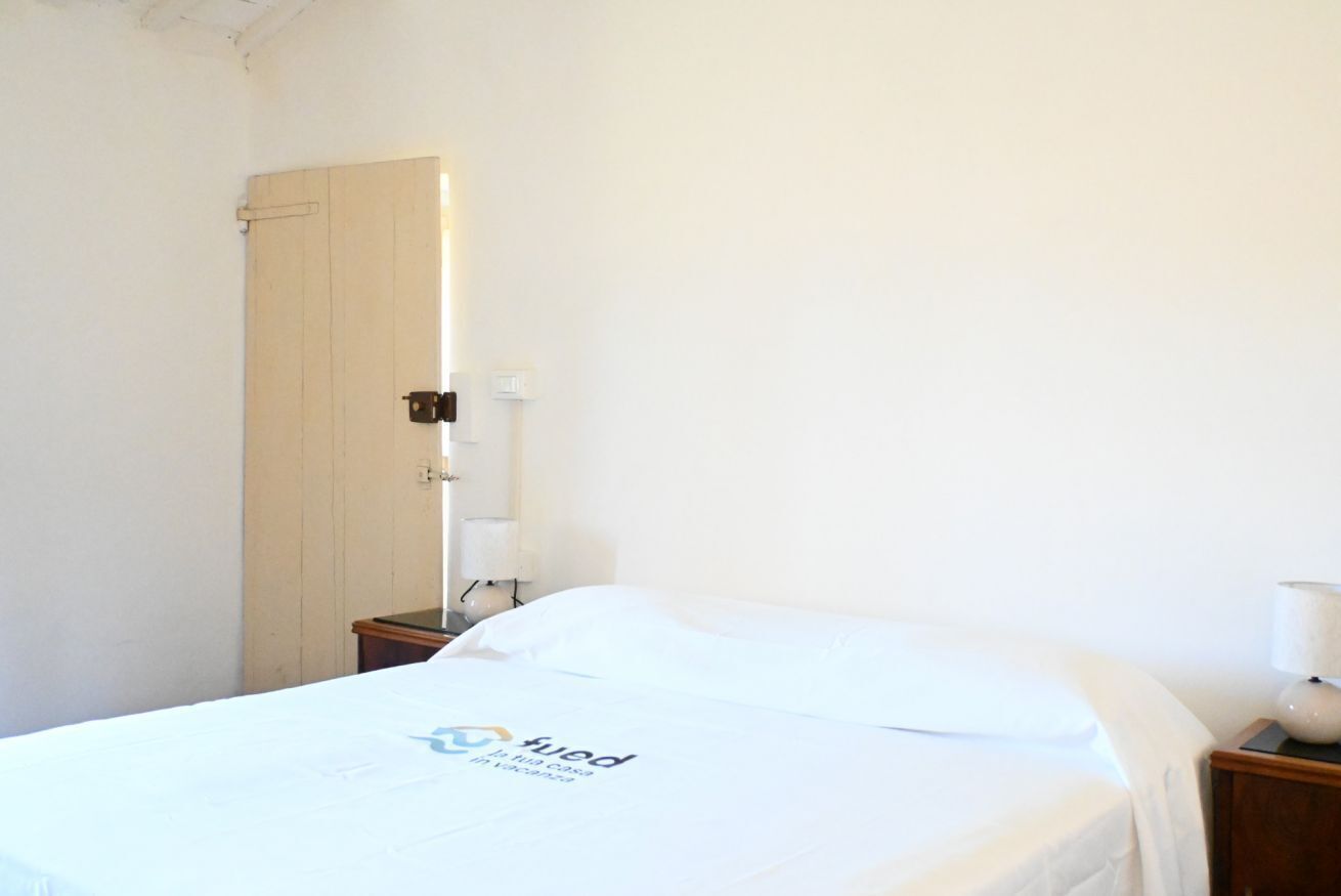 A single bed with a white bedspread, a wooden nightstand with a lamp, and a door with a light switch.