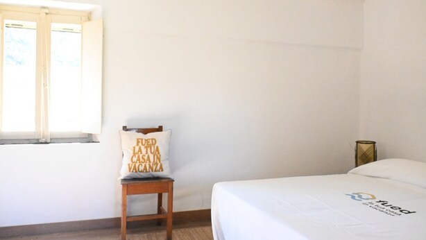 Un dormitorio con una cama, una silla, una mesita y una ventana.