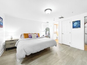 Un dormitorio con cama, mesita de noche, lámpara y una puerta que da a otra habitación.