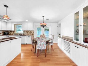 Una cocina con armarios blancos, una mesa de comedor de madera, sillas estampadas y un candelabro.