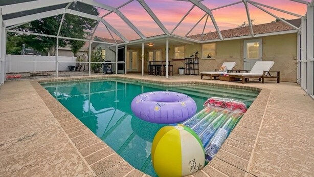 Ein überdachter Pool mit aufblasbaren Spielsachen, eine Terrasse mit Sitzgelegenheiten und Blick auf den Sonnenuntergang.