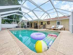 Una piscina techada con pelotas de playa inflables, un patio con sillas y una casa al fondo.