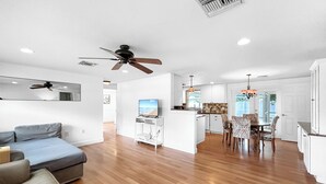 Ein modernes Wohnzimmer mit einer Couch, einem Deckenventilator und einer Küchenzeile mit Esstisch und Stühlen.