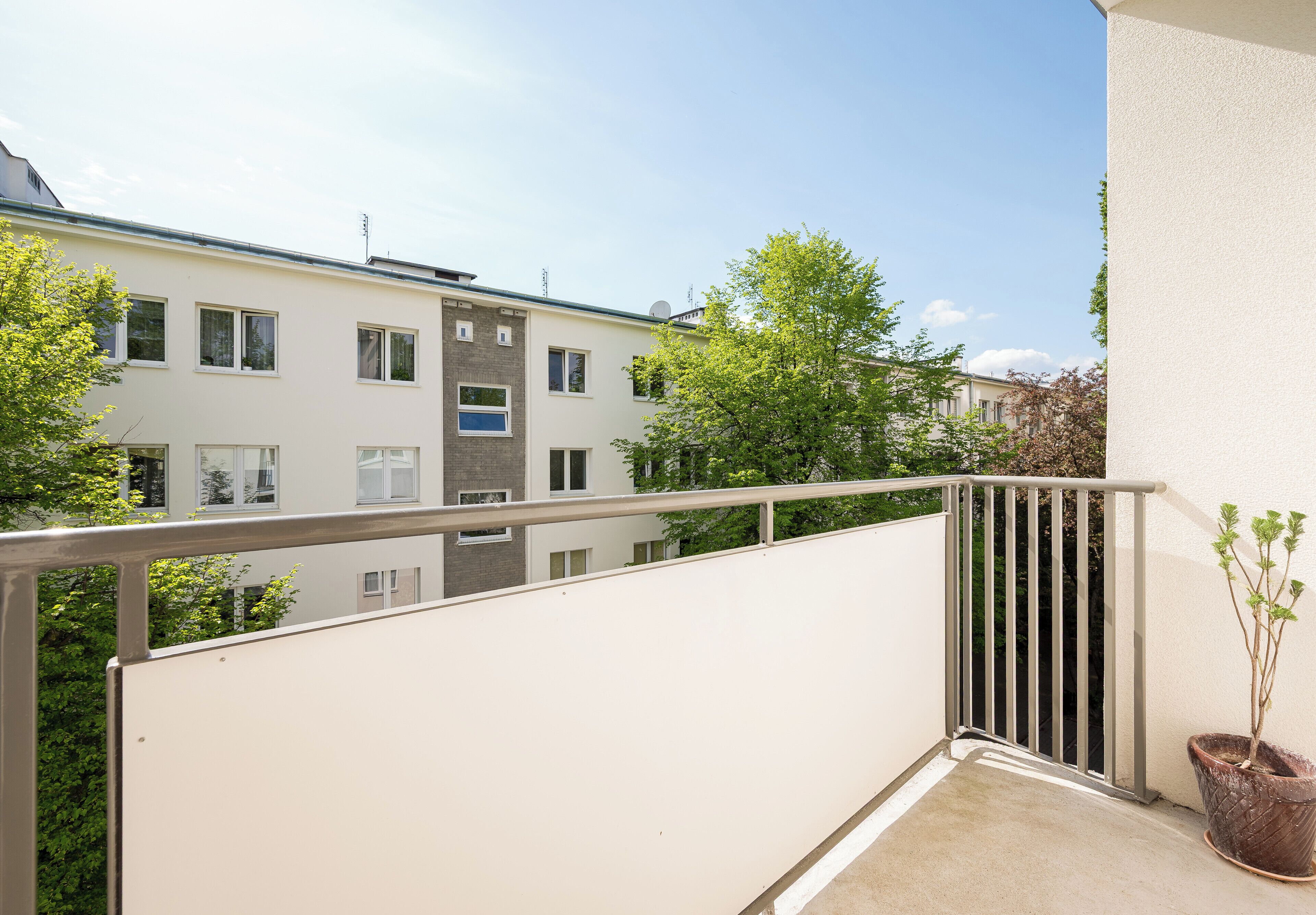 A balcony with a metal railing, a potted plant, and a view of neighboring buildings.