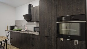 A modern kitchen with dark wood cabinets, a built-in oven, and a microwave. - Winogrady Nature Escape Apartment (Poznań)