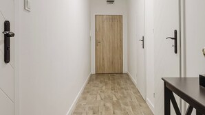 A narrow hallway with white walls, a wooden door at the end, and a wooden floor. - Winogrady Nature Escape Apartment (Poznań)