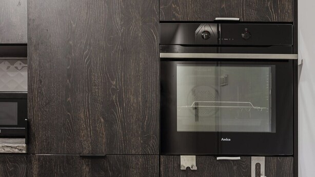 A modern kitchen with dark wood cabinetry, a built-in oven, and a microwave. - Winogrady Nature Escape Apartment (Poznań)