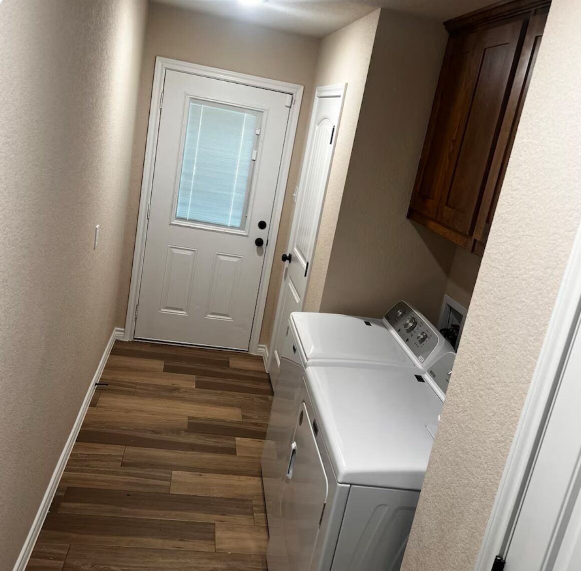 A laundry room with a door, wooden flooring, and a washing machine.