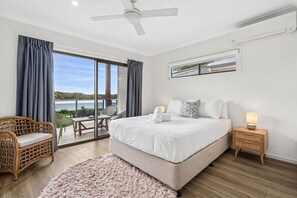 Un dormitorio con una cama grande, vistas al exterior, un ventilador de techo y una mesita de noche con lámpara.