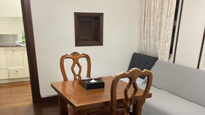 Ein Essbereich mit einem Holztisch und Stühlen, einem kleinen Fenster mit Jalousien und einer Couch im Hintergrund.