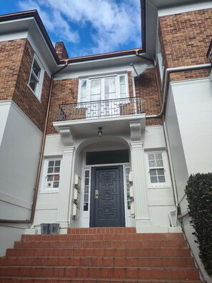 Un bâtiment à deux étages avec une porte d’entrée bleu foncé, des fenêtres à cadre blanc et une façade en briques.