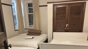 Ein Schlafzimmer mit zwei Einzelbetten, einem Holzschrank und einem Fenster mit Vorhängen.