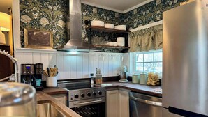 Una cocina con estufa, horno y lavavajillas de acero inoxidable, encimeras de madera y una ventana con cortinas.