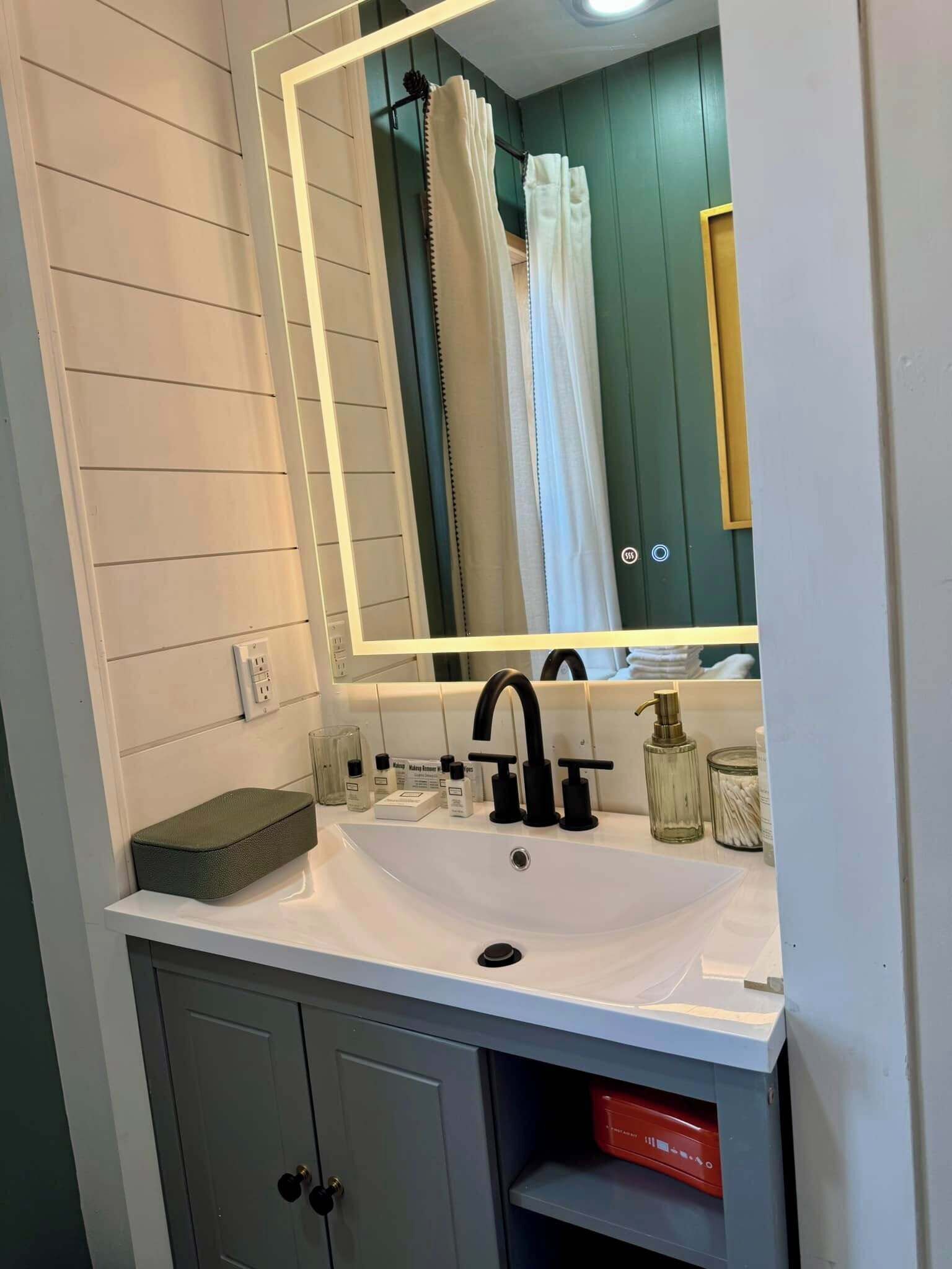 A bathroom with a white sink, black faucet, and a mirror with a white frame. There is a green door and a white towel rack.