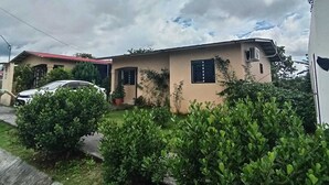 A two-story house with a red roof, a small garden, and a parked car. - Copeyhousechiriquí (Volcán)