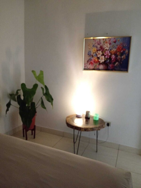 Una habitación con una planta en maceta, una mesita redonda con una lámpara y un cuadro en la pared.